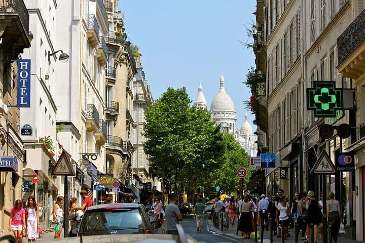 A popular street of Montmartre full of people with the basilica of “sacred heart” in the back ground