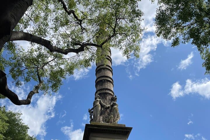 statue around a column and trees in front